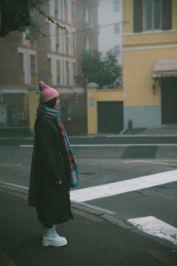 Pembe şapkalı ve eşarplı bir kadın şu anda caddeyi geçerken etrafını dikkatlice dolaşıyor.