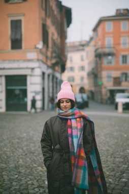 Zarif, pembe şapkalı ve eşarplı bir kadın büyüleyici bir kaldırım taşının üzerinde mutlu bir şekilde duruyor.