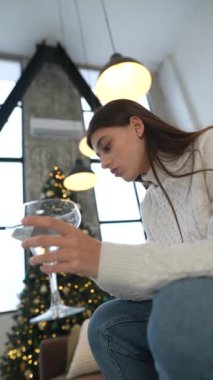 Dalgın bir kadın zarif bir şekilde elinde bir martini bardağı tutuyor. Etrafı şenlikli bir dekor ve ılık bir aydınlatmayla çevrili.