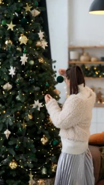 Neşeli bir kadın, güzel bir Noel ağacını sıcak ve davetkar bir ortamda renkli süslerle süslüyor.