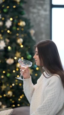 Genç bir kadın, güzel dekore edilmiş Noel ağacının yanında bayram neşesini somutlaştıran şenlikli bir içkiden hoşlanır.