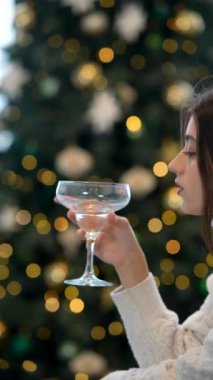 Güzel dekore edilmiş bir Noel ağacının yanında bir kadeh şenlikli neşeyle kadeh kaldıran bir kadın.
