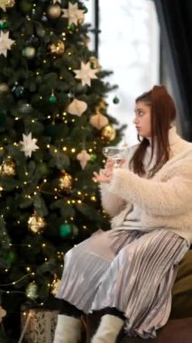 Güzel dekore edilmiş bir Noel ağacının yanında neşeyle oturan genç bir kadını gösteren huzurlu bir tatil anı.
