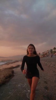 Genç bir kadın gün batımının güzel ve huzurlu manzarasının tadını çıkarırken sahilde sakin bir şekilde dolaşır.