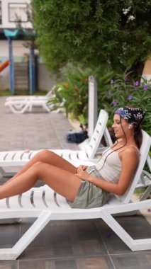 Genç bir kadın, güneşli havuz kenarında boş zamanlarının tadını çıkarıyor. Sıcak ve huzurlu yazları kucaklıyor.