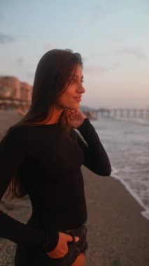 Genç bir kadın güzel bir gün batımında sahilde sakin bir akşam yürüyüşü yapıyor.