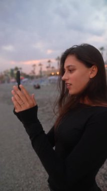 Bir kadın kumsalda gün batımının tadını çıkarırken bu değerli anı akıllı telefon cihazıyla yakalıyor.