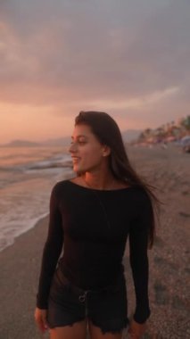 Bir kadın kumsalda neşeyle nefes kesici bir gün batımı yaşıyor. Huzurlu ve huzurlu bir atmosfer yaratıyor.