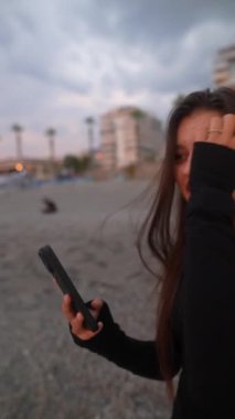 Düşünceli bir kadın kıyıda durup dikkatlice uzaklığa bakar ve huzurlu bir yansıma anı yakalar.