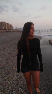 Huzurlu ve huzurlu bir an güzel bir gün batımında kumsalda rahatça gezinen neşeli bir kadını yakalıyor.