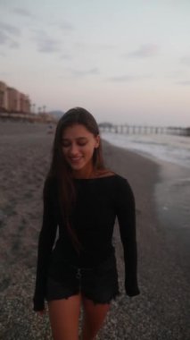 Bir kadın güzel günbatımında kumlu bir sahilde rahatça geziniyor, zamanın huzurlu anının tadını çıkarıyor.