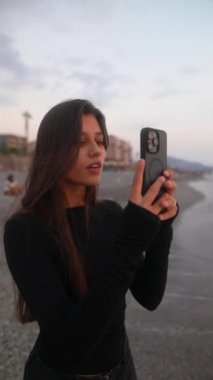 Gün batımında sahilde neşeyle selfie çeken birini gösteren güzel ve huzurlu bir an yakalıyor.