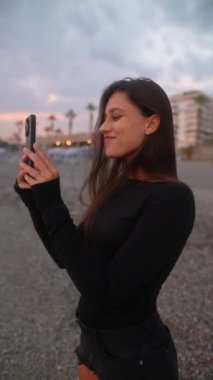 Güzel bir sahilde, sakin ve sakin bir alacakaranlık saatinde bir kadın akıllı telefonuyla meşgul oluyor.