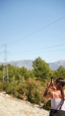 Bir kadın açık mavi bir gökyüzünün altında fotoğraf çekerken nefes kesici ve nefes kesici güzellikte manzaralar yakalıyor.