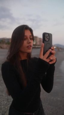 Genç bir kadın, gün batımında plajda güzel bir anı yakalar. Rahatlama ve güzelliği yansıtır.