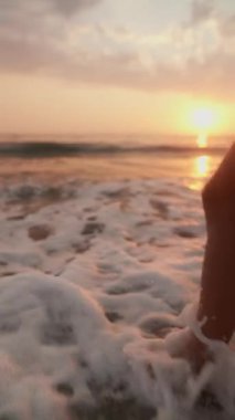 Gün batımında sıcak kumda bir ayak huzurlu bir kumsalın sakin okyanus dalgalarında sakin bir atmosfer yaratır.