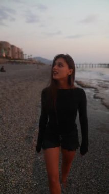 Gün batımında güzel, sakin bir plajda yürüyen genç bir kadın sükunetin gerçek özünü yakalıyor.