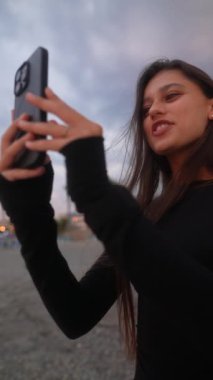 Neşeli bir insan, akıllı telefonuyla canlı bir selfie çekerken güneşli bir deniz sahili anının derinden tadını çıkarıyor.