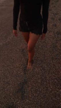 Güneş batarken, bir kadın kumsalda yalınayak yürüyor, etrafındaki doğal güzellikleri kucaklıyor.