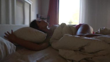 Bir kadın rahat yatağında uyanır, yumuşak bir yastığı sımsıkı tutar. Sıcak güneş ışığı pencereden içeri doğru akar.