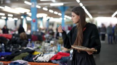 Genç bir kadın lezzetli bir şeyler atıştırırken giysi ve daha fazlası ile dolu market tezgahlarına göz gezdiriyor.