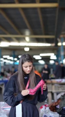 Genç bir kadın hareketli bir pazarda renkli bir eşarbı inceliyor, alışveriş kültürünün özünü yakalıyor.