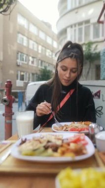 Genç bir kadın, canlı ve canlı bir şehir atmosferiyle çevrili iken açık havada yemek yemekten zevk alıyor.