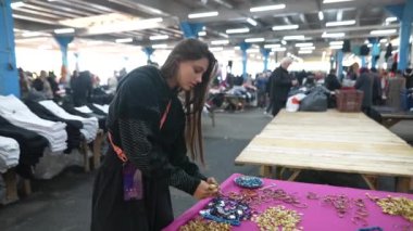 Genç bir kadın, canlı bir markette müşterilerle dolu çeşitli aksesuarları hevesle inceliyor.
