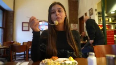 Genç bir kadın, sıcak ve davetkar bir restoran ortamında yemeğinin tadını çıkarıyor.