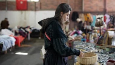 Odaklanmış ve kararlı genç bir kadın canlı, hareketli bir vintage pazarında çeşitli eşsiz parçaları dikkatle inceliyor.