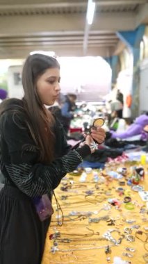 Bir kadın, canlı ve hareketli bir pazar ortamını keşfederken çeşitli mücevher parçalarını dikkatlice inceler.