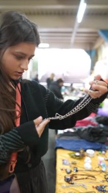 Genç bir kadın, eşsiz mallar ve etkileşimlerle dolu hareketli bir pazarda çarpıcı bir gümüş kolyeyi inceliyor.