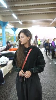 Zarif siyah giyinmiş şık bir kadın şehir piyasası atmosferini ve güncel moda eğilimlerini mükemmel bir şekilde somutlaştırıyor.