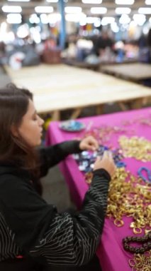 Genç bir kadın düşünceli ve titiz bir şekilde hareketli bir pazarda renkli ıvır zıvırlar serisi düzenliyor.