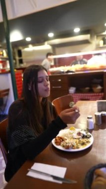Genç bir kadın sıcak ve davetkar bir restoran atmosferinde otururken gerçekten lezzetli yiyeceklerin tadını çıkarıyor.