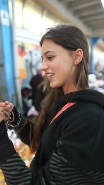 Gülümseyen genç bir kadın canlı ve canlı bir pazarda çeşitli renkli mücevherler sergiliyor.