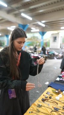 Bir kadın canlı bir markette güzel mücevherleri inceliyor, alışveriş için çeşitli el sanatları sergiliyor.