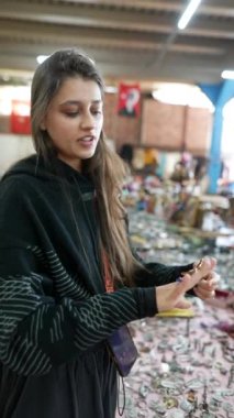 Bir kadın, eşsiz sanatsal eşyalar ve koleksiyon eşyalarıyla dolu canlı bir pazara rahatça göz atıyor.