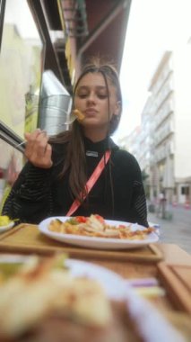 Bir kadın, keyifle lezzetli ve tatmin edici bir yemeğin tadını çıkarıyor. Tek başına, cadde kenarındaki bir kafede.
