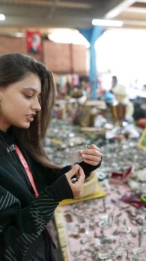 Hareketli ve hareketli bir pazarda, bir kadın birçok renkli eşya arasında güzel ve karmaşık mücevherleri dikkatle inceler.