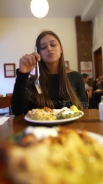 Genç bir kadın, neşeli ve hayat dolu bir restoran ortamında lezzetli yemeklerinin tadını çıkartıyor.