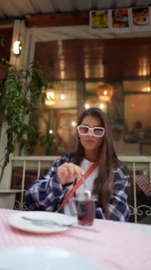 Tarz sahibi genç bir kadın sıcak bir kafede içkisini yudumluyor, çağdaş moda ve ambiyansı kucaklıyor.