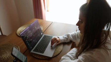 Genç bir kadın konforlu bir evde laptopunu aktif olarak kullanıyor, üretkenliği ve yaratıcılığı kişisel dokunuşlarla somutlaştırıyor.