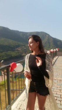 Şık bir insan balkonda poz veriyor, göz kamaştırıcı dağ manzaraları ve canlı şenlik dekorasyonları vurguluyor.