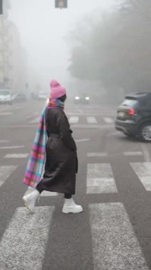 Şık bir şahsiyet sisli bir sokakta zarif bir şekilde yürüyor, şehir manzarası içinde güzel bir kış modası sergiliyor.