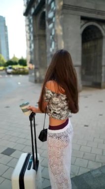 Canlı bir sahne, elinde kahve ve bavuluyla telefon görüşmesi yapan genç bir kadını yakalıyor.