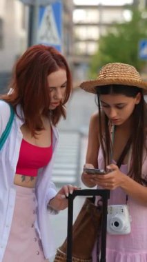 İki genç kadın birlikte seyahat ederken akıllı telefonlarıyla birbirlerine neşeyle bağlanıyorlar.