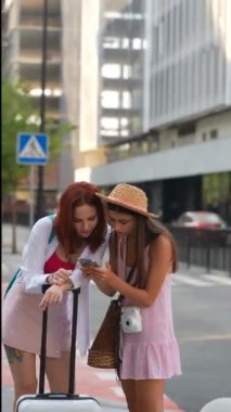 Bir grup genç kadın dışarıda telefonlarını kontrol ederken birlikte mutlu bir şekilde vakit geçiriyorlar.