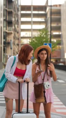 Renkli bavulları olan iki şık arkadaş yaz kıyafetleri içinde heyecanlı şehir maceralarının tadını çıkarıyorlar.