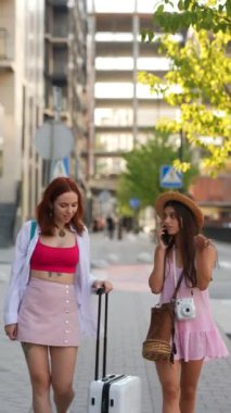 İki şık ve modaya uygun arkadaş ellerinde bavullarını taşırken canlı şehir manzarasını zevkle keşfediyorlar.